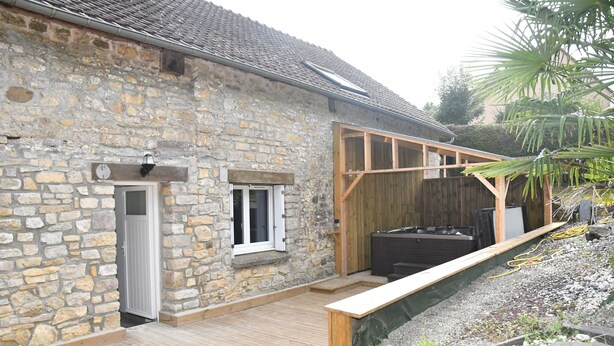 Ein Steinhaus mit einer Holzterrasse, einem Holzzaun und einem Garten mit Steinen und Pflanzen.