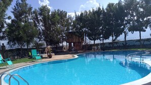 Una piscina de borde curvo, rodeada de sillas de descanso y una pequeña estructura de madera.