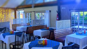 Un restaurante con mesas cubiertas de manteles blancos y posavasos azules, bancos de madera y un extintor en la pared.