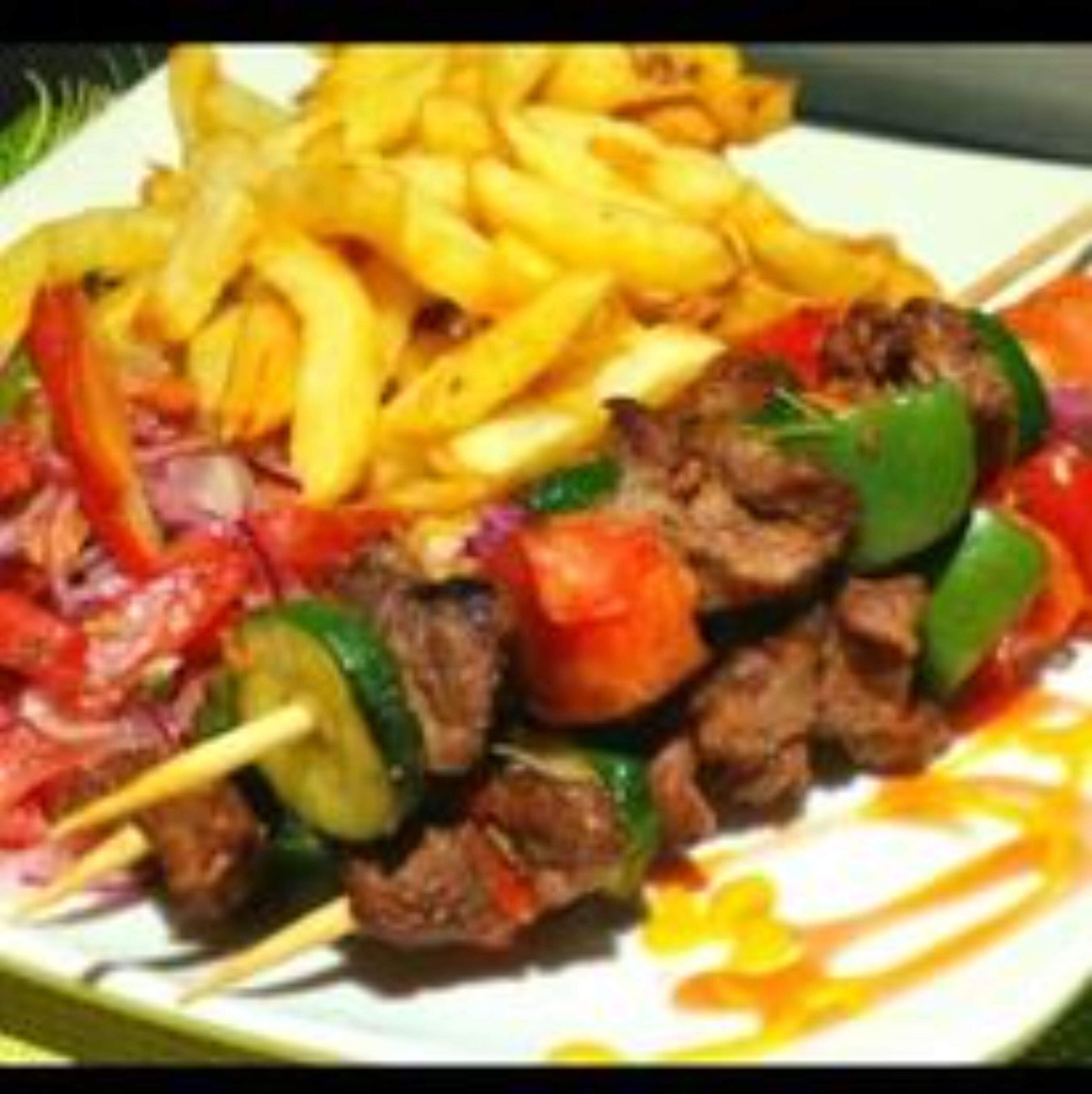 Une assiette de viande grillée en brochettes, accompagnée de légumes et de frites.