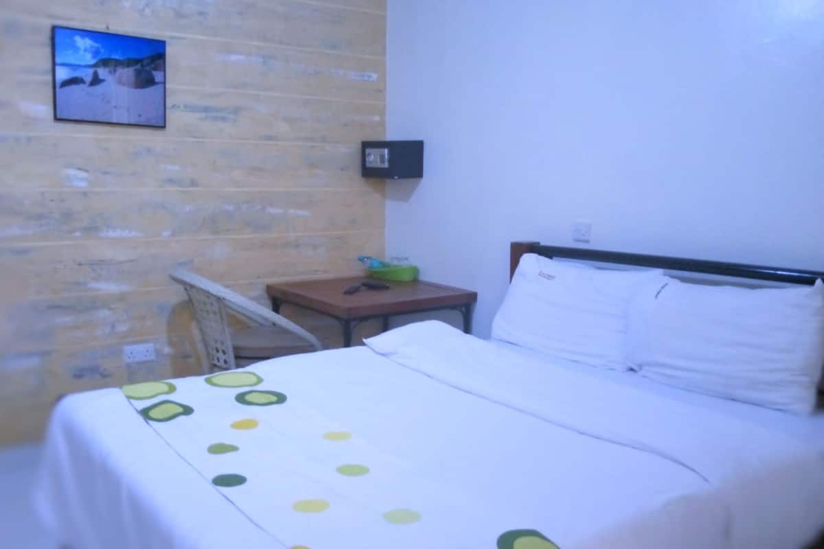 Une chambre d’hôtel avec un lit, une petite table, une chaise, un téléviseur fixé au mur et un tableau accroché au mur.