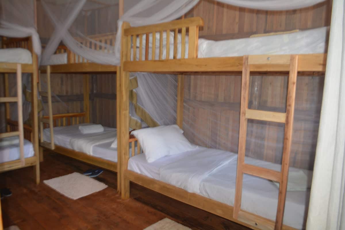 A room with bunk beds, wooden flooring, and mosquito netting.