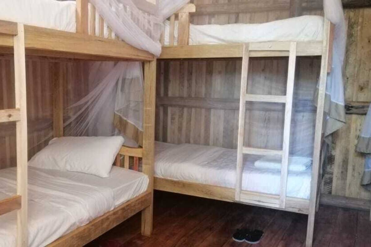 A wooden bunk bed room with mosquito netting, a wooden floor, and a small stool.