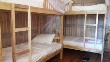 A wooden bunk bed room with mosquito netting, a wooden floor, and a small stool.