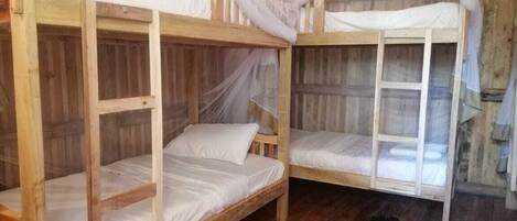 A wooden bunk bed room with mosquito netting, a wooden floor, and a small stool.