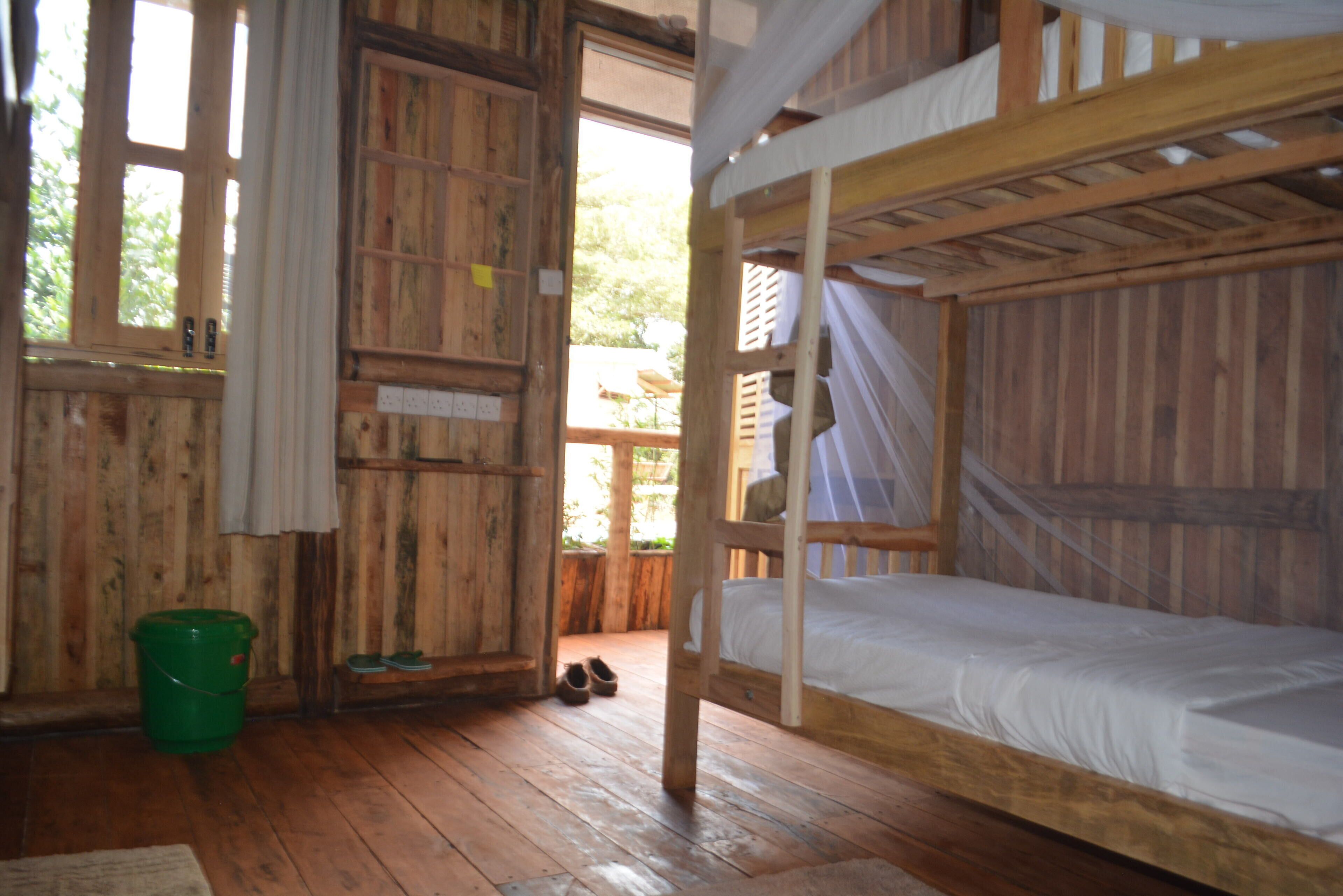 A wooden cabin with a bunk bed, a green bucket, and a pair of shoes on the floor.