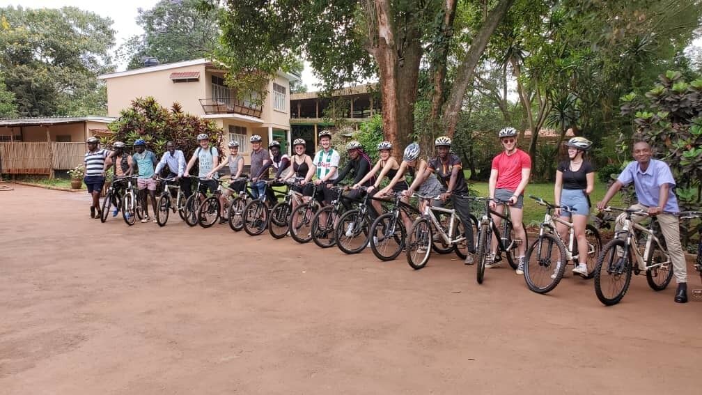 A group of people on bicycles lined up in an outdoor area with a building in the background.