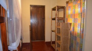 Un pasillo estrecho con una puerta de madera, un estante de madera y una cortina colorida.