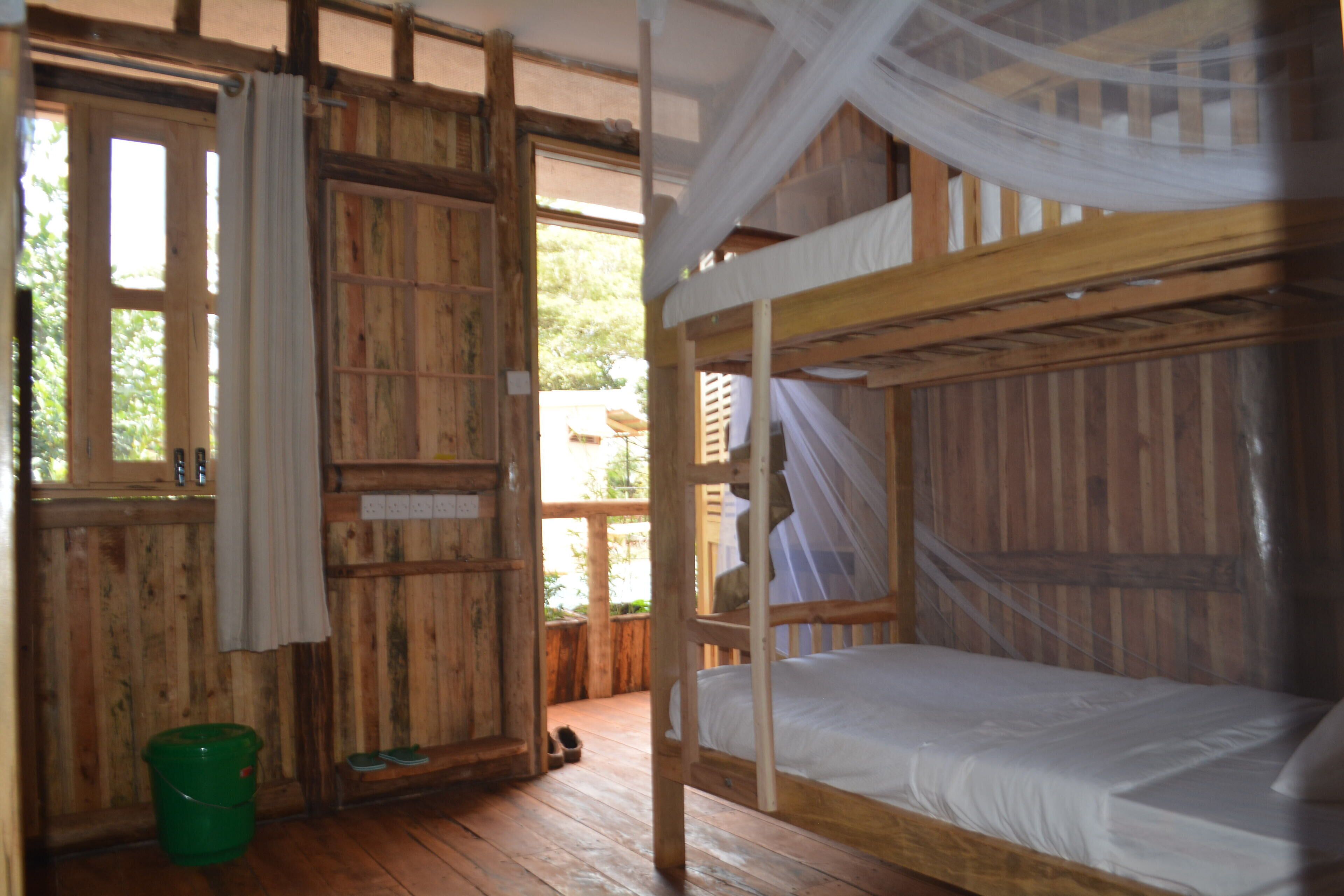 A rustic wooden room with a bunk bed, a green bucket, and a window with curtains.