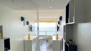 A modern, minimalist interior with a central corridor leading to a seating area and a view of the sea.