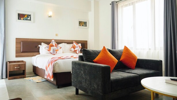 A hotel room with a bed, a grey sofa, a small table, and a window with curtains. - Eliper Hotel (Gatura)