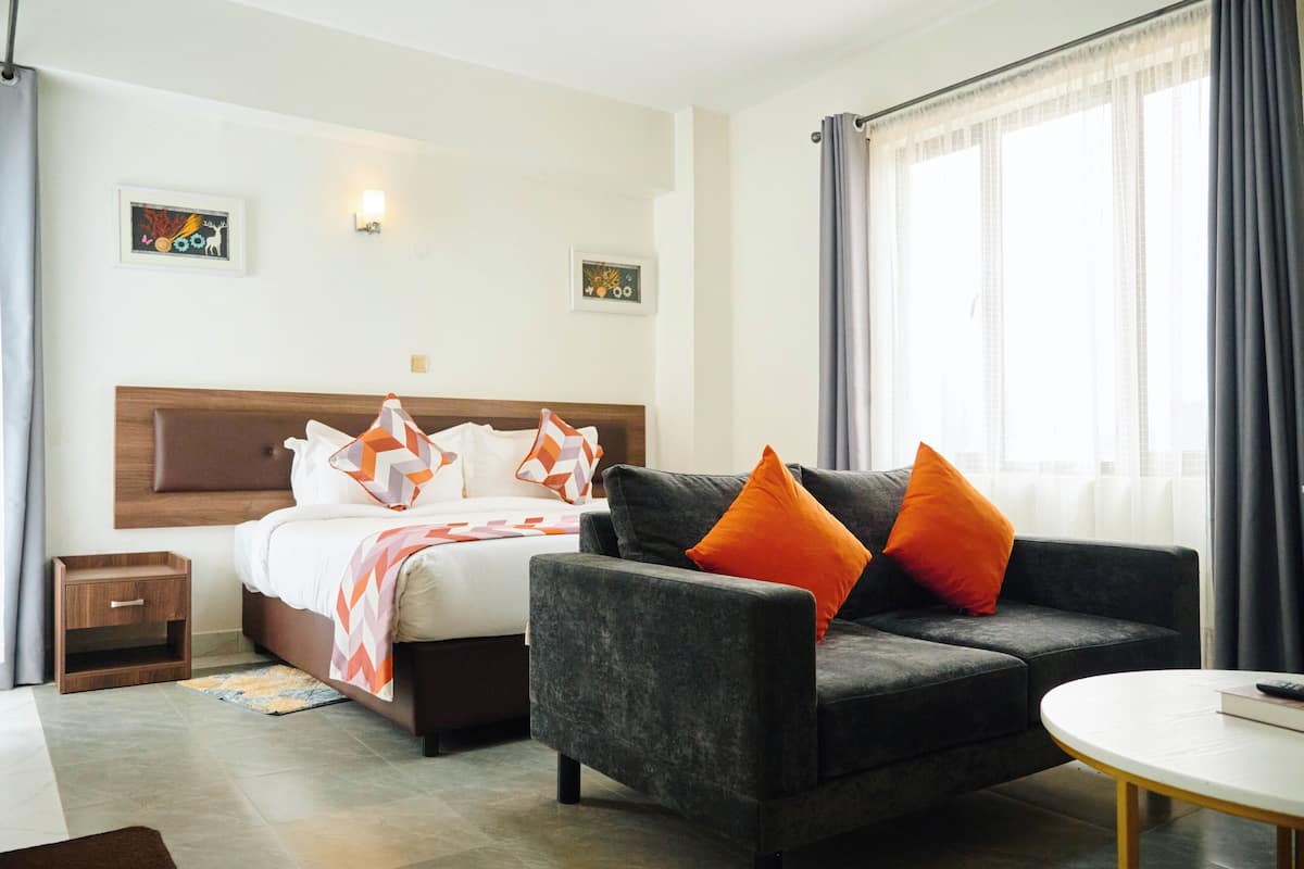 A hotel room with a bed, a grey sofa, a small table, and a window with curtains.