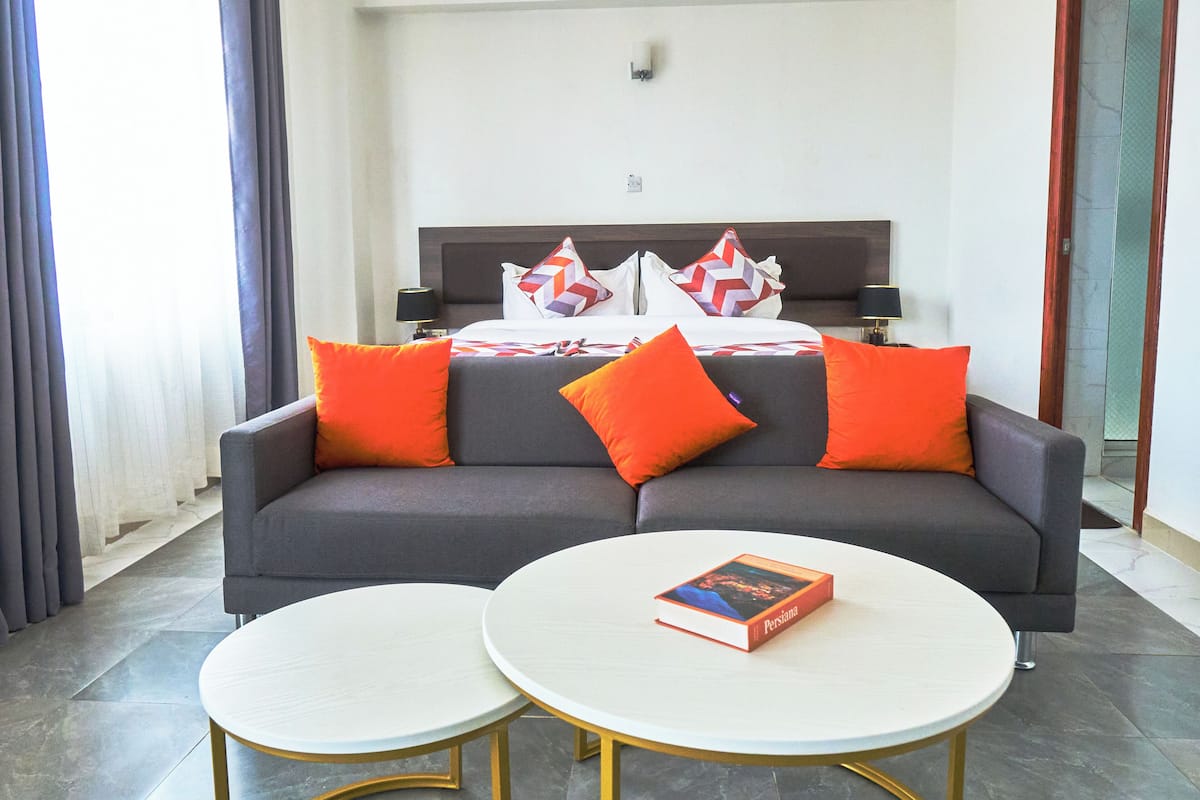 A modern hotel room with a grey sofa, two round white tables, and a book on one table.