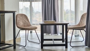 A room with two chairs and a table, large windows with curtains, and a view of buildings outside. - Eliper Hotel (Gatura)