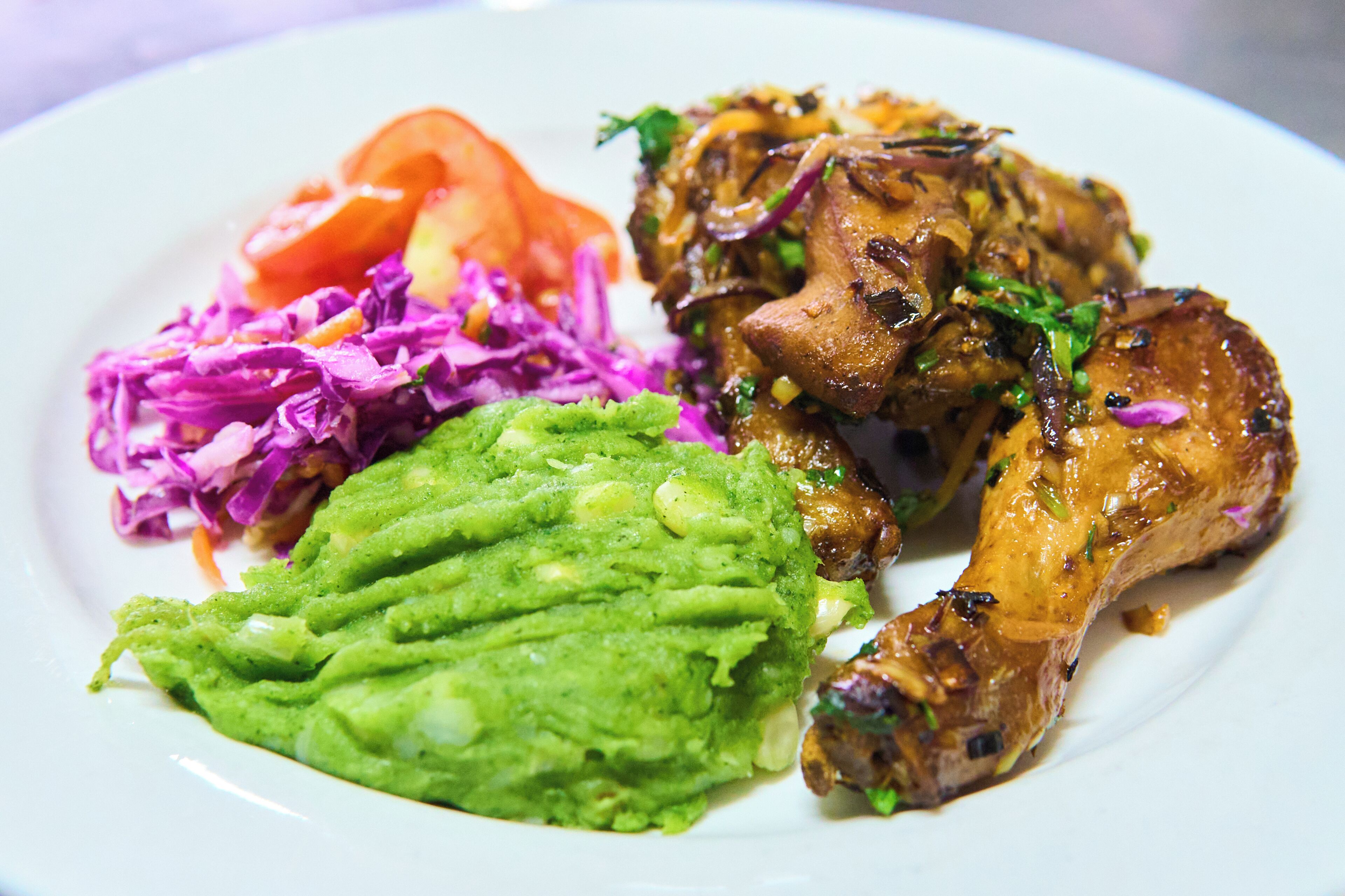 En tallrik med ett grillat kycklinglår, en portion röd kål som tillbehör och en skål guacamole.