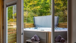 A spa area with a hot tub, two small benches, and a wooden deck. - Cozy cabin minutes from restaurants & entertainment and surrounded by nature.   (Sevierville)