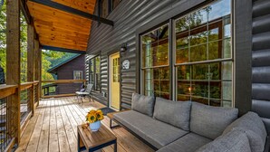 A log cabin with a wooden deck, a sofa, and a table with a vase of sunflowers. - Cozy cabin minutes from restaurants & entertainment and surrounded by nature.   (Sevierville)