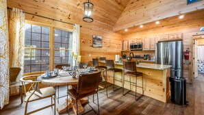 A wooden cabin interior with a dining area, kitchen, and a sign that says "happy". - Cozy cabin minutes from restaurants & entertainment and surrounded by nature.   (Sevierville)
