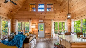 A cozy cabin interior with a wooden ceiling, a sofa, a dining table, and a kitchen area. - Cozy cabin minutes from restaurants & entertainment and surrounded by nature.   (Sevierville)