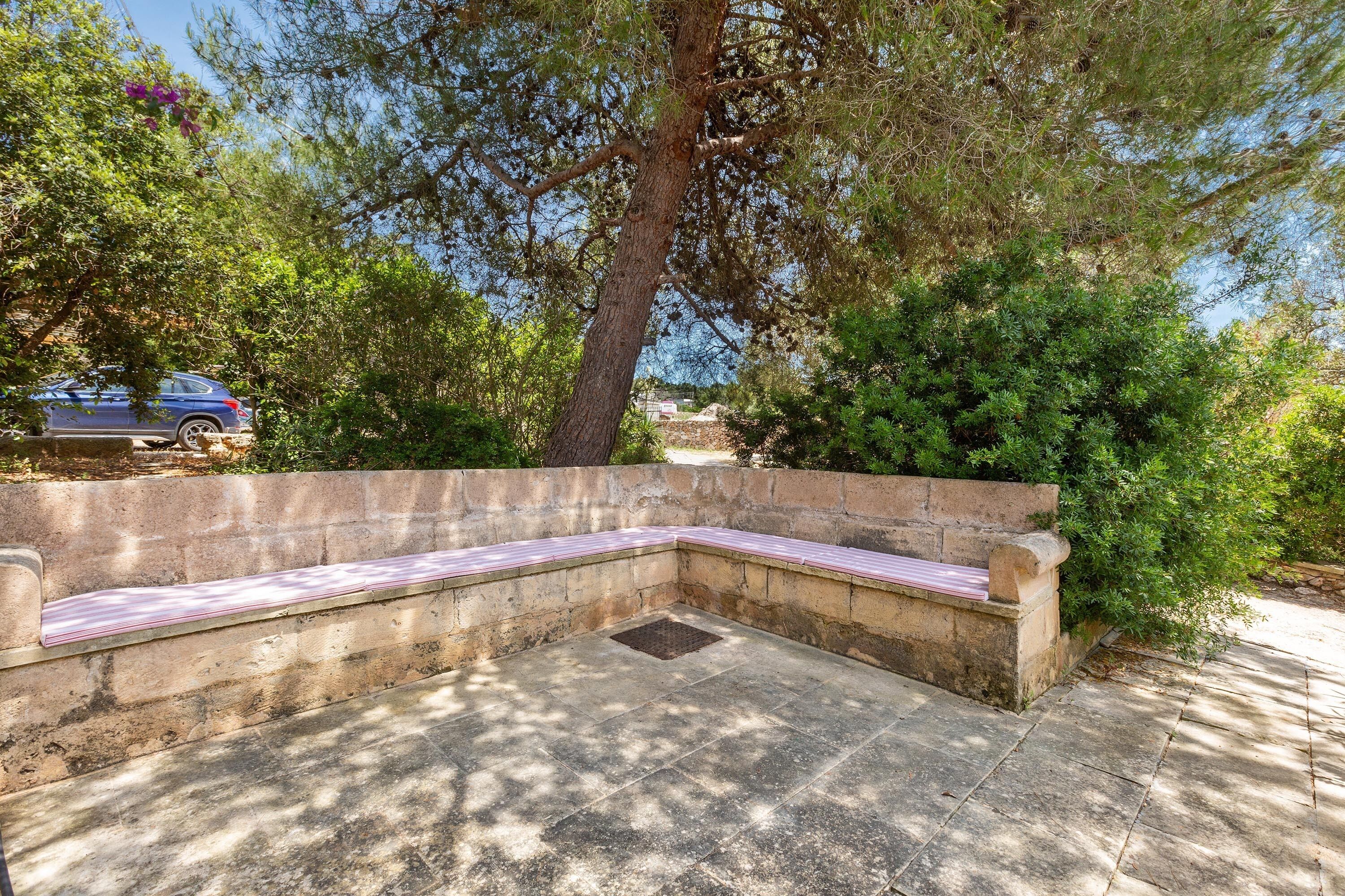 A stone bench with a metal grate, surrounded by trees and a stone wall.