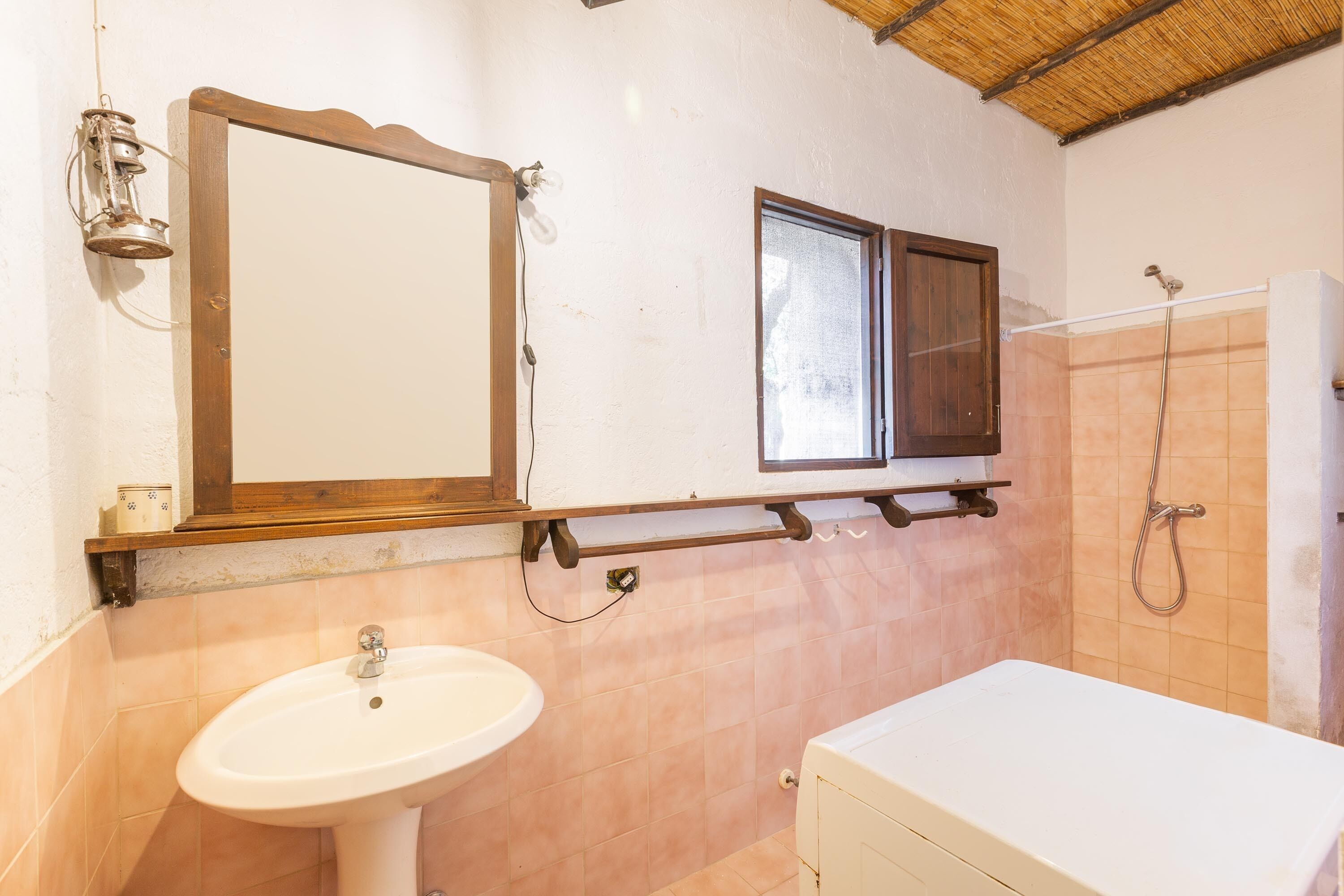 A bathroom with a sink, mirror, window, shower, and wooden shelf.