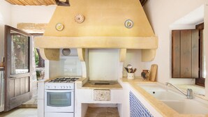 Une cuisine équipée d’une cuisinière à gaz, d’un four, d’un évier et d’une grande hotte aspirante au-dessus.