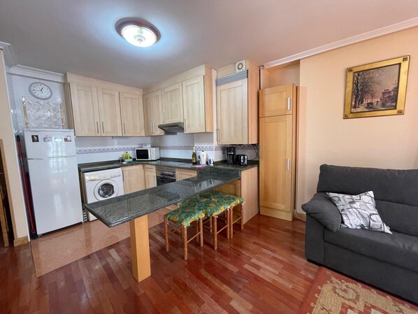 A compact kitchen with a dining area, a washing machine, and a sofa.