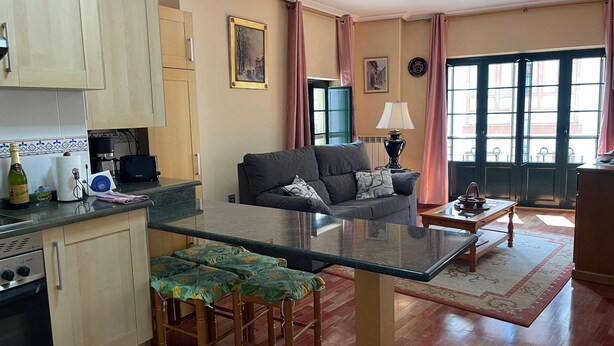 Una sala de estar acogedora con un sofá, una mesa de centro de vidrio y una zona de cocina con estufa y armarios.