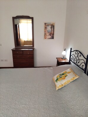 Quarto com cama, penteadeira, espelho, mesa de cabeceira com abajur e um quadro na parede.