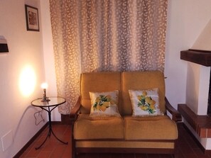 A room with a sofa, a small table with a lamp, and a patterned curtain. - Apartment Lemons La Burraia (GAMBASSI TERME)