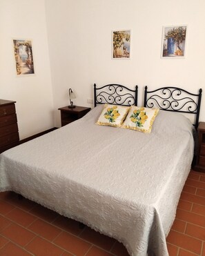 A bedroom with a bed, two nightstands, a dresser, and three wall-mounted paintings. - Apartment Lemons La Burraia (GAMBASSI TERME)