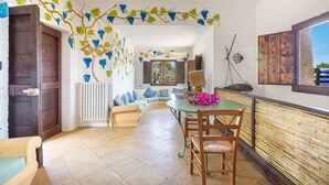 A cozy room with a wooden door, a sofa with cushions, a dining table with chairs, and a wall with grapevine decorations. - 3503 PJE - Casa La Pergola by Barbarhouse (Castrignano del Capo)