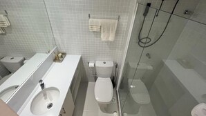 A bathroom with two sinks, a toilet, a glass-enclosed shower, and a towel rack. - Vista mar no Costa Azul (Costa Azul Salvador)