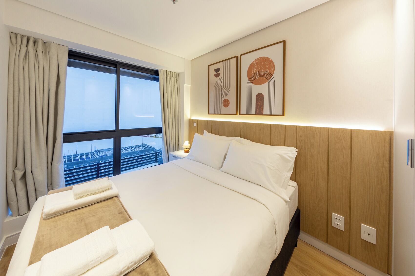 Ein Hotelzimmer mit einem großen Bett, Blick auf eine Baustelle und zwei gerahmten Kunstwerken an der Wand.