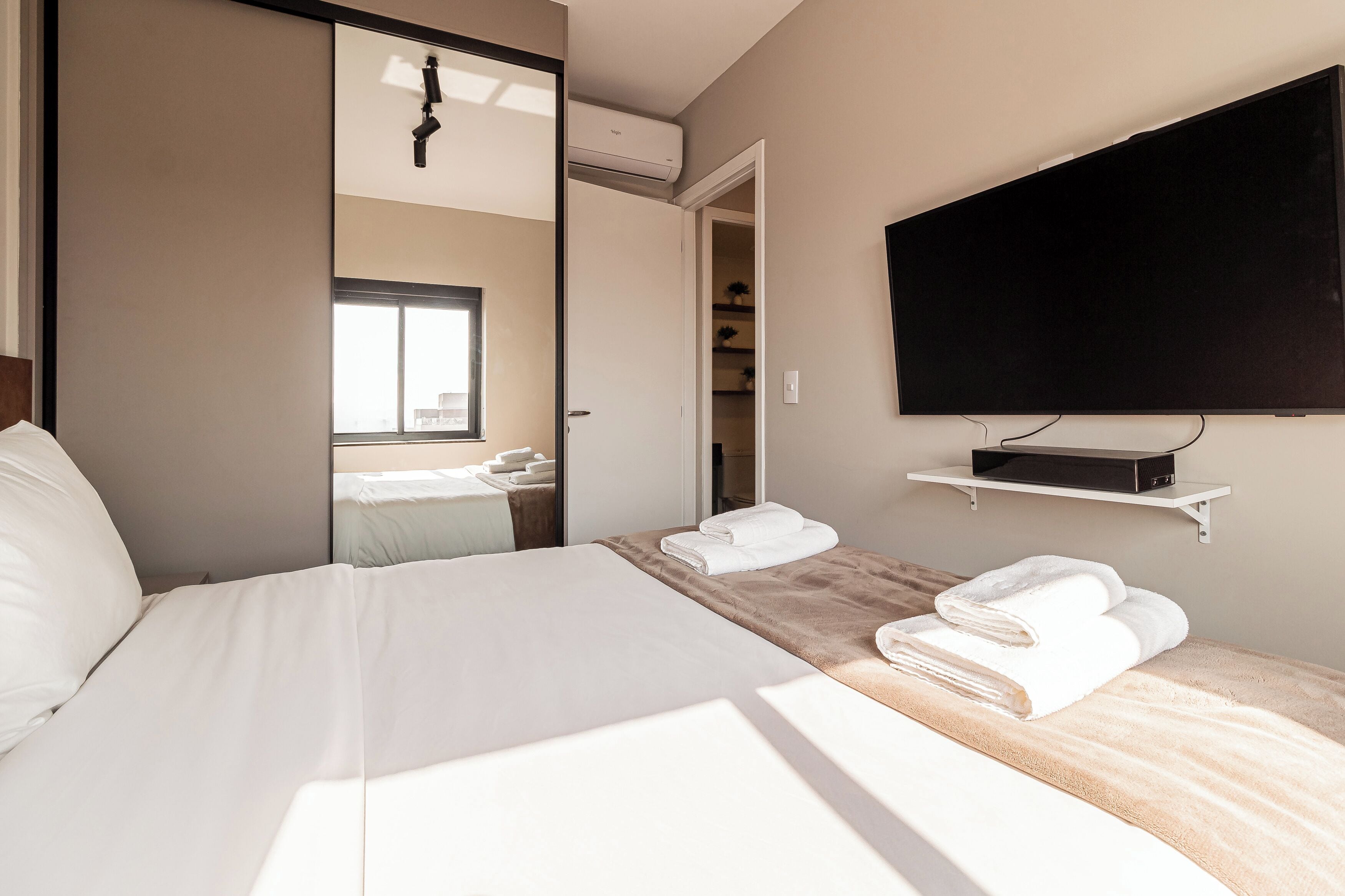 Une chambre d’hôtel avec un lit, un téléviseur fixé au mur et une salle de bain visible à travers une porte ouverte.