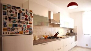 Een keuken met een koelkast vol magneten, witte kastjes, een gasfornuis en een rode hanglamp.
