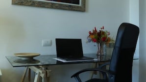 Een werkplek met een laptop, een bloemenvaas, een zwarte stoel en een schilderij aan de muur.