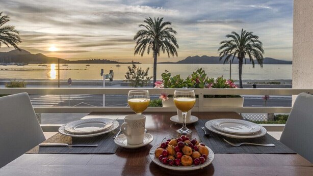 Une table dressée pour deux, avec vue sur le coucher de soleil sur l’eau, les palmiers et une assiette de fruits.