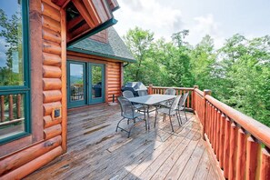 A wooden deck with a table and chairs, a barbecue grill, and a view of a forested area. - Wild View Lodge, Picturesque mountain escape, Hot Tub, Spacious living room (Bartlett)