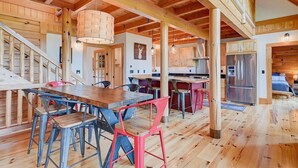 En rummelig spiseplads med et træbord og stole, et køkken med stålemfangere, og en trappe til en etage ovenover.