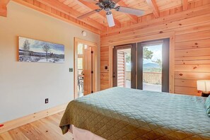 A bedroom with a bed, wooden walls, a ceiling fan, and a door leading to a balcony with a view. - Wild View Lodge, Picturesque mountain escape, Hot Tub, Spacious living room (Bartlett)