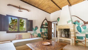 A rustic room with a wooden table, a sofa, a window with cactus artwork, and a fireplace. - 3504 PJE - Casa Fico D'india by Barbarhouse (Castrignano del Capo)