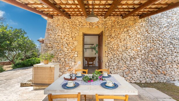 A stone-walled outdoor dining area with a table set for four, wooden chairs, and a hanging light fixture. - 3504 PJE - Casa Fico D'india by Barbarhouse (Castrignano del Capo)