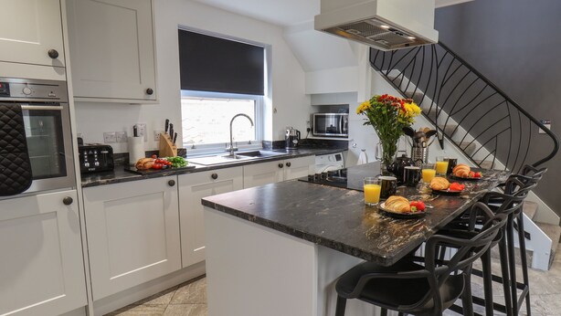 A modern kitchen with white cabinets, a central island with bar stools, a built-in oven, and a window above the sink.