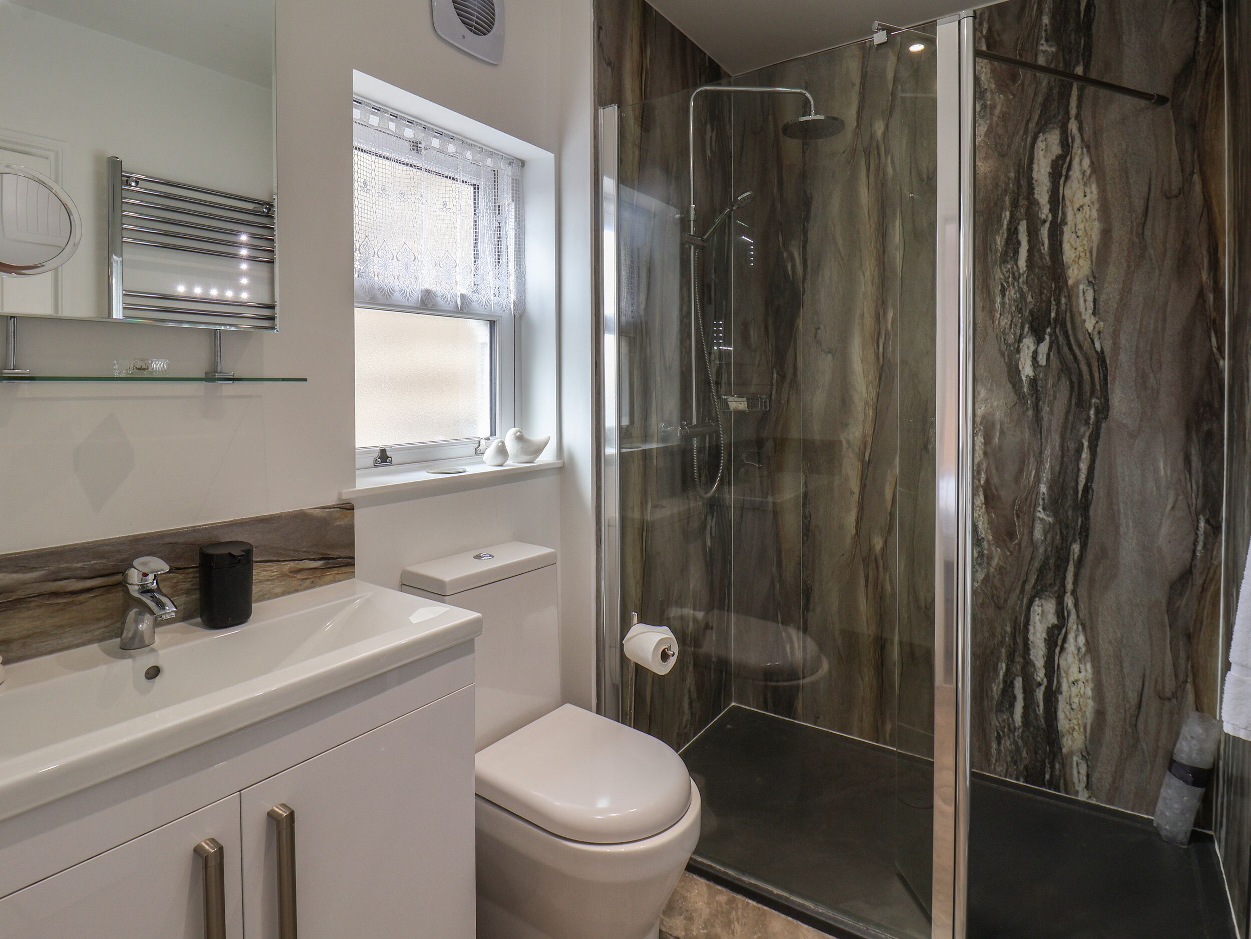 A modern bathroom with a glass-enclosed shower, a toilet, and a sink with a mirror above it.