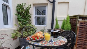 An outdoor patio with a round table, chairs, a potted plant, and a wicker basket.