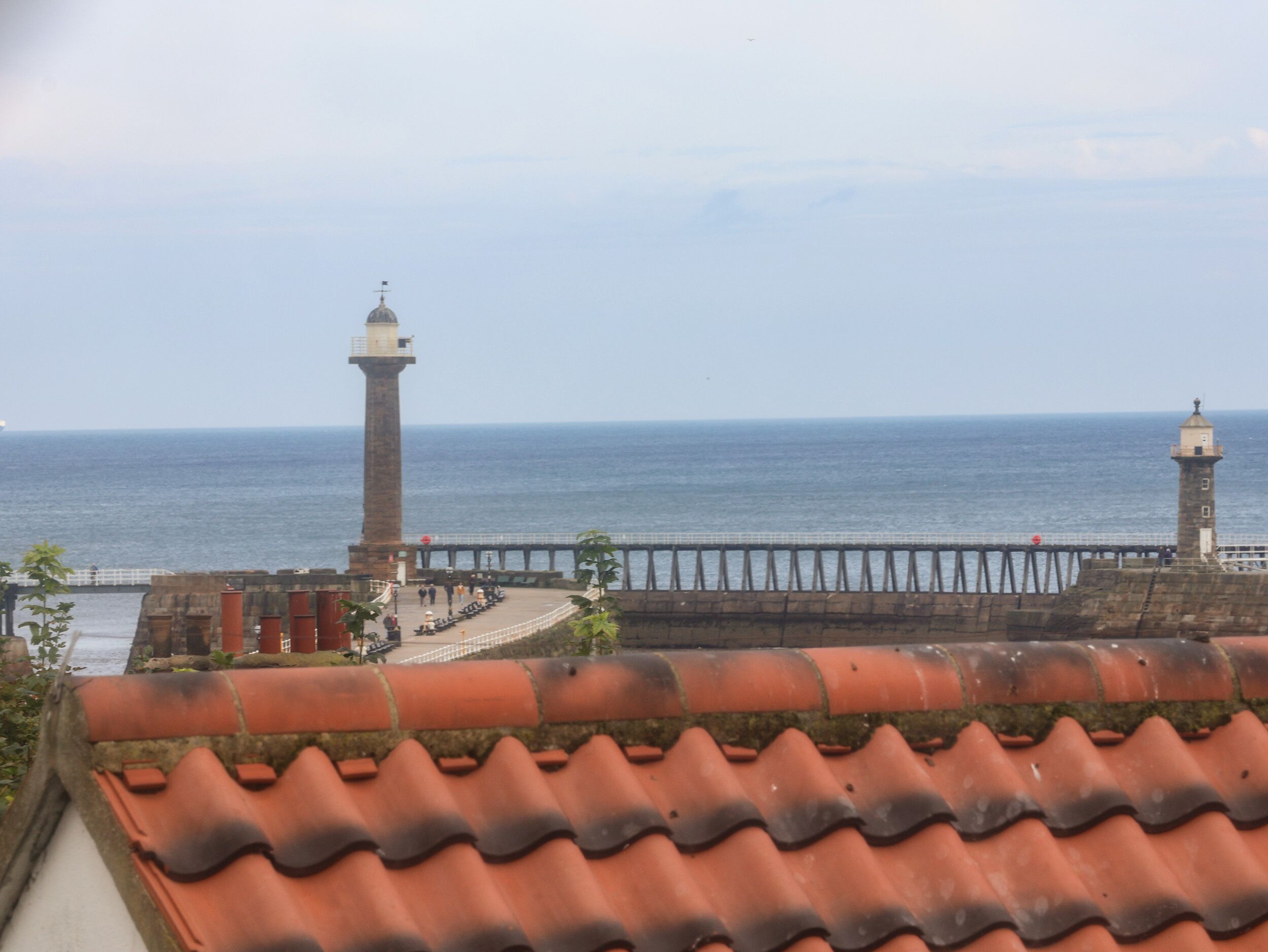 A coastal view with a lighthouse and a pier extending into the sea.