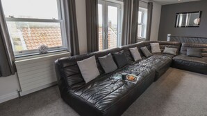 A modern living room with a black leather sofa, grey cushions, and a small table with a tray of fruit.