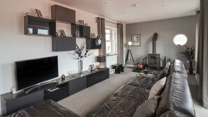 A modern living room with a large flat-screen TV, leather sofas, a fireplace, and a large window.