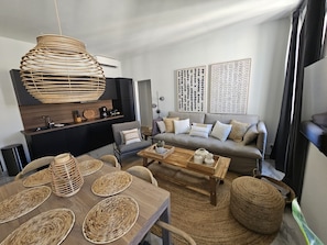 Ein modernes Wohnzimmer mit einem Holzesstisch, gewebten Untersetzern, einer Couch mit Kissen und einer Pendelleuchte.